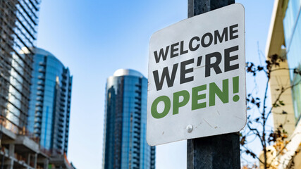 Welcome We're Open Worn Sign in Downtown city setting