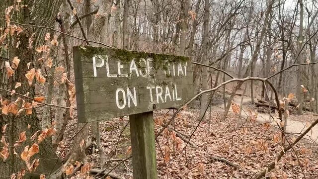 This panning video shows an outdoors safety sign that reads - please stay on trail. Warning sign discouraging people from getting lost or danger in the forest
