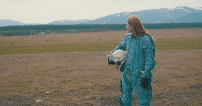 Woman astronaut wearing space suit is looking around terrain.