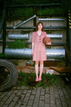 Girl in a pink dress with a basket ball in a yard