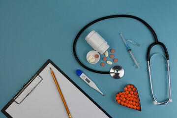 fanndoscope, pills, disposable syringe, ampoule with medicine, thermometer, pencil and blank paper on a blue background top view