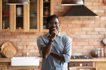 Happy homeowner. Smiling millennial african american man posing for portrait at modern kitchen interior. Successful young black guy hipster just moved in new home house look at camera enjoy wellbeing
