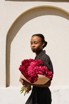 City portrait of a beautiful black girl in a polka dot dress with a bouquet of peony flowers