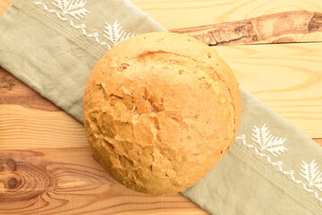 One loaf of delicious white bread with a linen napkin on a wooden table, close-up, top view.