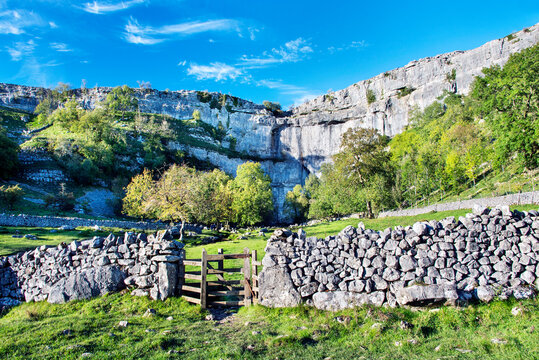 Malham Cove in the Yorkshire Dales with blue sky, drystone wall and gate.