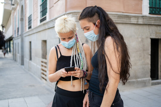 Lesbian Couple With Blue Masks And Phone Outdoors.