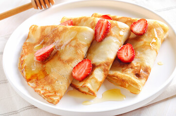 Homemade thin pancakes with strawberry slices and honey