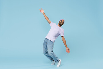 Full length young cool smiling happy funny unshaven black african man 20s wearing violet t-shirt hat glasses standing on toes leaning back dancing isolated on pastel blue background studio portrait. - Powered by Adobe