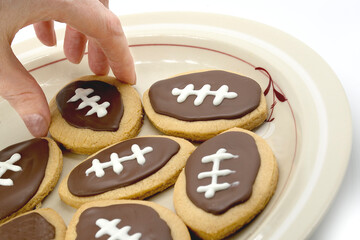 Football shape cookies on plate. Hand taking cookie from plate. Home made cookies concept. American sport concept. Super Bowl party cookies.