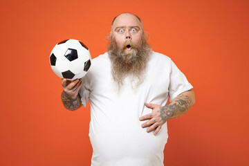 Fat shock confused man pudge football fan in white t-shirt cheer up support favorite team with soccer ball omg look camera isolated on orange background studio. People sport leisure lifestyle concept.