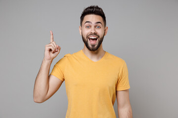 Young caucasian bearded happy insighted smart intelligent man 20s wearing casual yellow basic t-shirt holding index finger up with great new idea isolated on grey color background studio portrait.