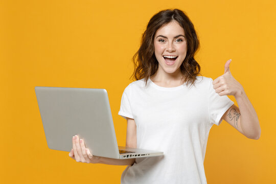 Young smiling freelancer copywriter caucasian student woman in white basic t-shirt hold laptop pc computer chat browsing show thumb up like gesure isolated on yellow orange background studio portrait.