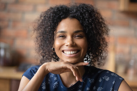 Headshot portrait of happy joyful young african american female show beautiful teeth in white cheerful smile. Adorable laughing millennial black woman looking at camera flirtatiously touching chin