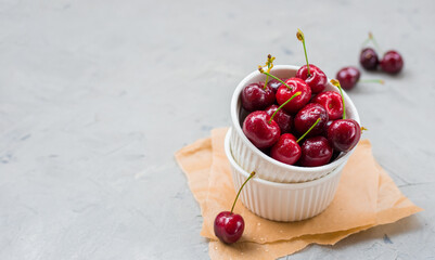 White bowl full of sweet cherries on gray stone background. Rustic style. Food banner, Copy space.