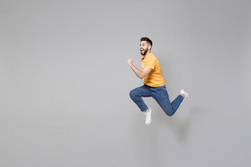 Fototapeta na wymiar Full length of young bearded sport active student hurrying man 20s in yellow basic t-shirt jump high running away fast do winner gesture clench fist isolated on grey color background studio portrait..