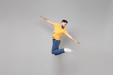 Fototapeta na wymiar Full length of young bearded student smiling happy cheerful overjoyed man 20s in yellow basic t-shirt jump high looking aside flying outstretched hands isolated on grey background studio portrait