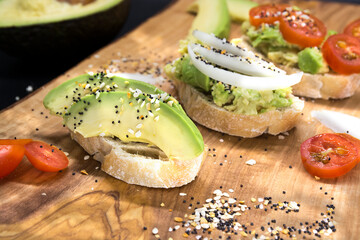 Healthy avocado toasts, appetizers with seeds and tomatoes on wooden board, dark background. Avocado sandwiches. Food photo, healthy food.