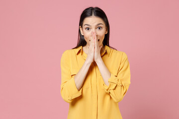 Young shocked surprised leader wondered confused brunette nice attractive latin woman 20s wear yellow casual shirt covering mouth with hands palms isolated on pastel pink background studio portrait.