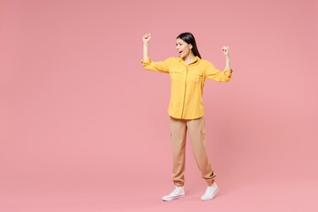 Full length of young smiling brunette excited overjoyed attractive latin woman 20s in casual yellow shirt do winner gesture clench fist celebrating isolated on pastel pink background studio portrait.