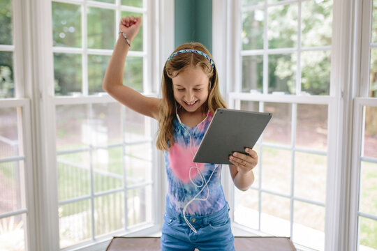 Beautiful young girl dancing while holding a computer tablet and listening to music