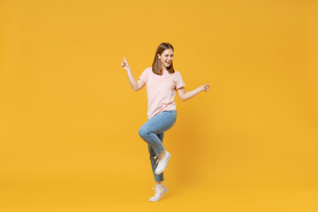 Full length of young caucasian happy satisfied excited woman 20s in casual basic pastel pink t-shirt, jeans pointing index fingers celebrating isolated on yellow color background studio portrait