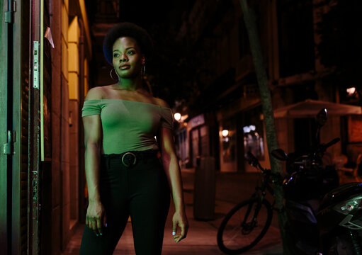 Woman with afro hair standing outdoors in the city in a summer night.