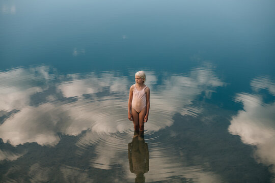 Little girl standing in the water where white clouds are reflected