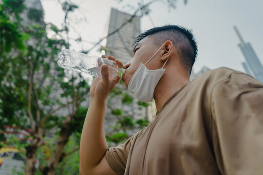 Young asian runner man putting off face mask while drinking water after finished running and working out. He wearing medical mask