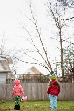 Pretty blond girl with yellow knit hat playing outside with her toddler friend on a chilly spring day