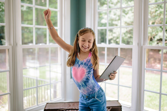 Beautiful young girl dancing while holding a computer tablet and listening to music