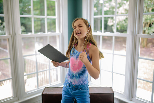 Beautiful young girl dancing while holding a computer tablet and listening to music