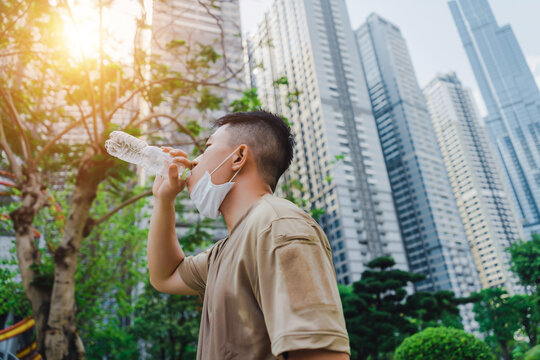 Young asian runner man putting off face mask while drinking water after finished running and working out. He wearing medical mask