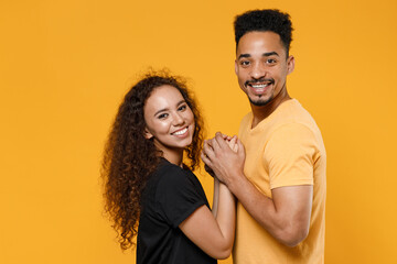 Fototapeta premium Young couple two friends together family smiling happy lovely cheerful african man woman 20s wearing yellow black t-shirt hugging holding hands isolated on orange color background studio portrait.