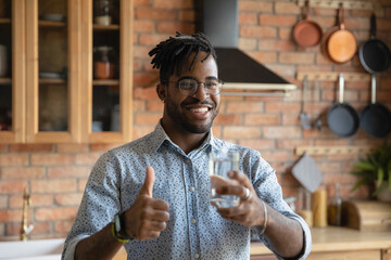 Take care of health. Portrait of active african male hipster at home kitchen recommend drink pure...