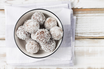 Coconut energy balls in a white cup on a light wooden background.