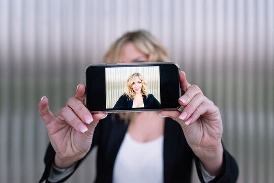 Attractive woman photographing and taking a selfie with her mobile phone. Cute middle-aged woman with blonde hair taking pictures of herself with her smart phone.