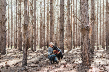 Woman cuddling belgian shepherd in forest