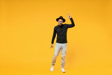 Full length young fun african man 20s wearing stylish black hat shirt eyeglasses doing winner gesture pointing index finger up look camera isolated on yellow orange color background studio portrait