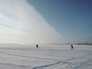Active elder people cross-country skiing on huge frozen lake during lovely winter sunset