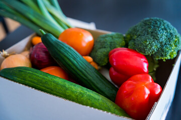 Set of different fresh vegetables in a cardboard box on a table. Home delivery of groceries during coronavirus quarantine. Broccoli, leek, cucumbers, bell peppers, tomatoes, onions bought.