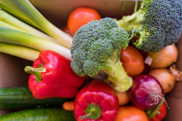 Set of different fresh vegetables in a cardboard box. Home delivery of groceries during coronavirus quarantine. Broccoli, leek, cucumbers, bell peppers, tomatos, onions bought in a supermarket.