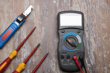 Multimeter and screwdrivers on the wooden workbench background. Electric tools.