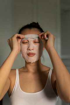 Portraiture of a young asian woman putting on a moisturised face-mask
