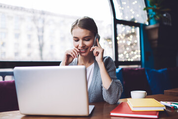 Cheerful woman with laptop making phone call