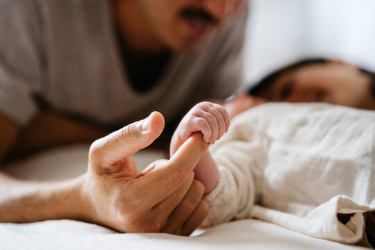 Close up of anonymous newborn baby holding unrecognizable's mother's finger on bed