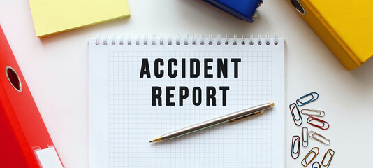 Notepad with text ACCIDENT REPORT on a white background, near document folder and office supplies.