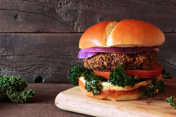Vegan bean and sweet potato burger with kale, onion and tomato. Close up against a dark wood background.
