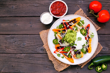 Healthy, plant based bell pepper nachos. Overhead view table scene on a dark wood background. Low carb, vegetarian diet.