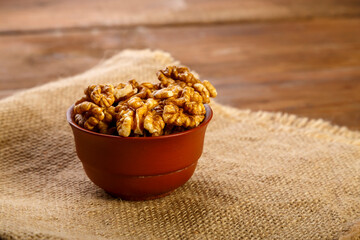 Walnuts in a clay cup on burlap on a wooden table.
