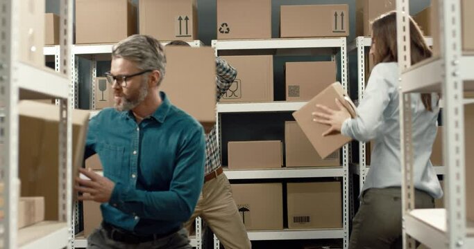 Three cheerful colleagues having fun dancing in warehouse with cardboard boxes in their hands celebrating successful business deal.